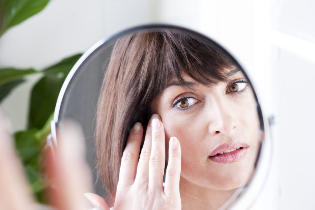 Woman looking at aging skin in mirror