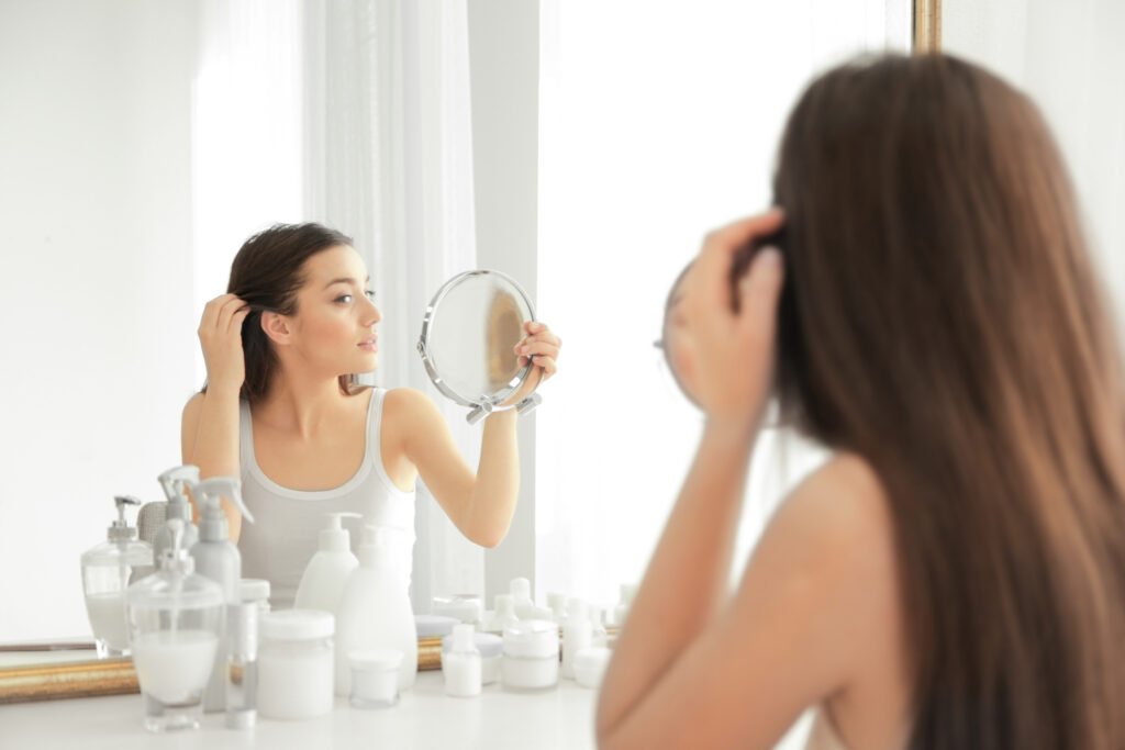 Woman looking at hair loss in mirror.