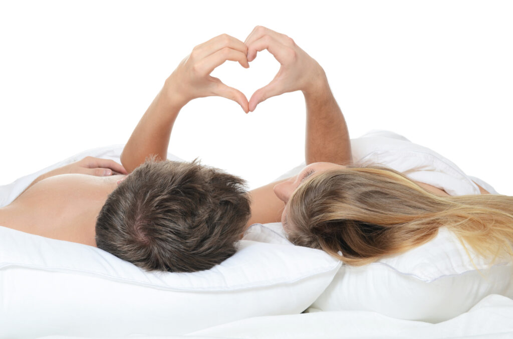 Healthy couple in bed making a heart with their hands. 